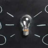 light bulb with surrounding idea bubbles on chalkboard